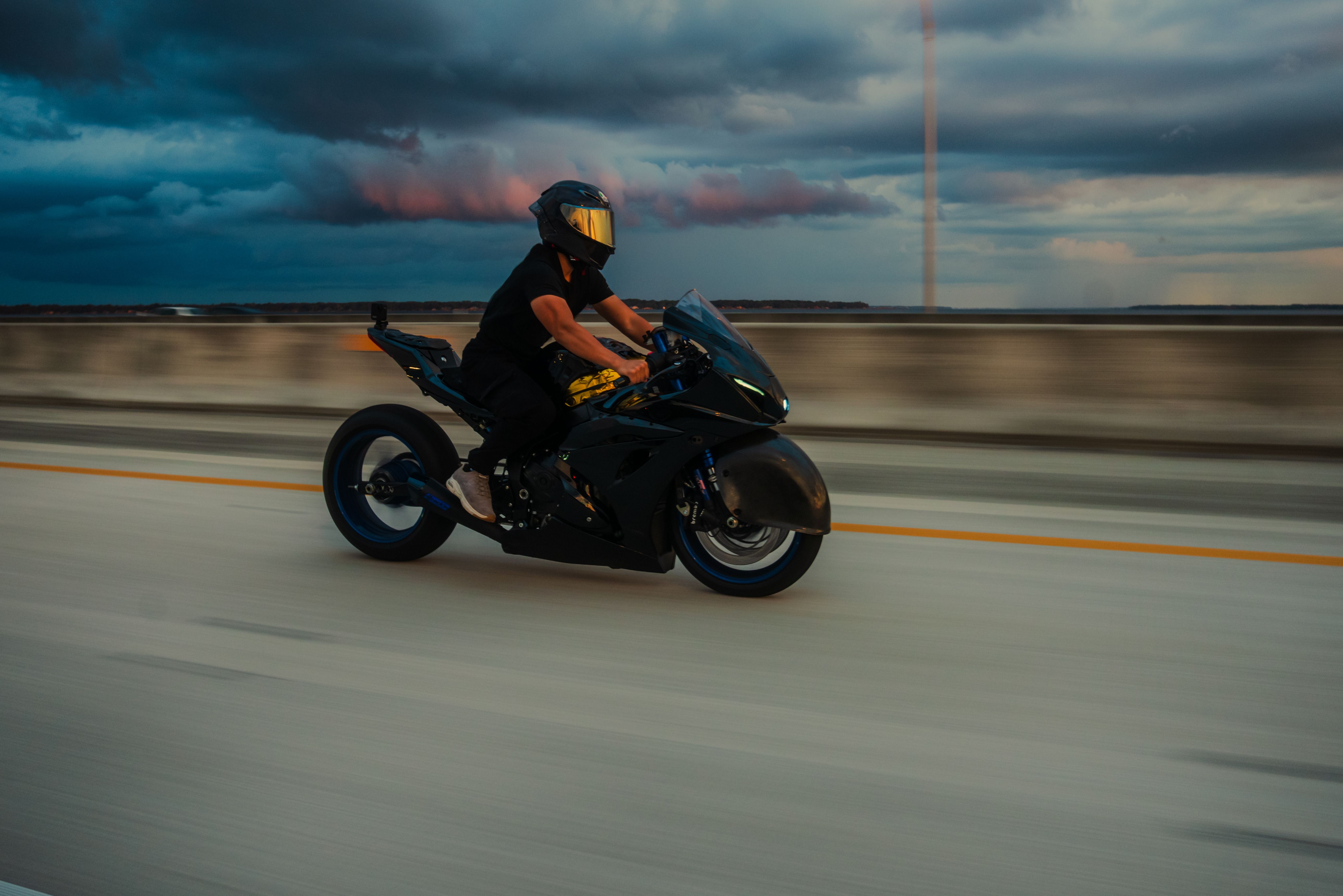 Motorcyclist riding fast on a highway beneath a dramatic cloudy sky