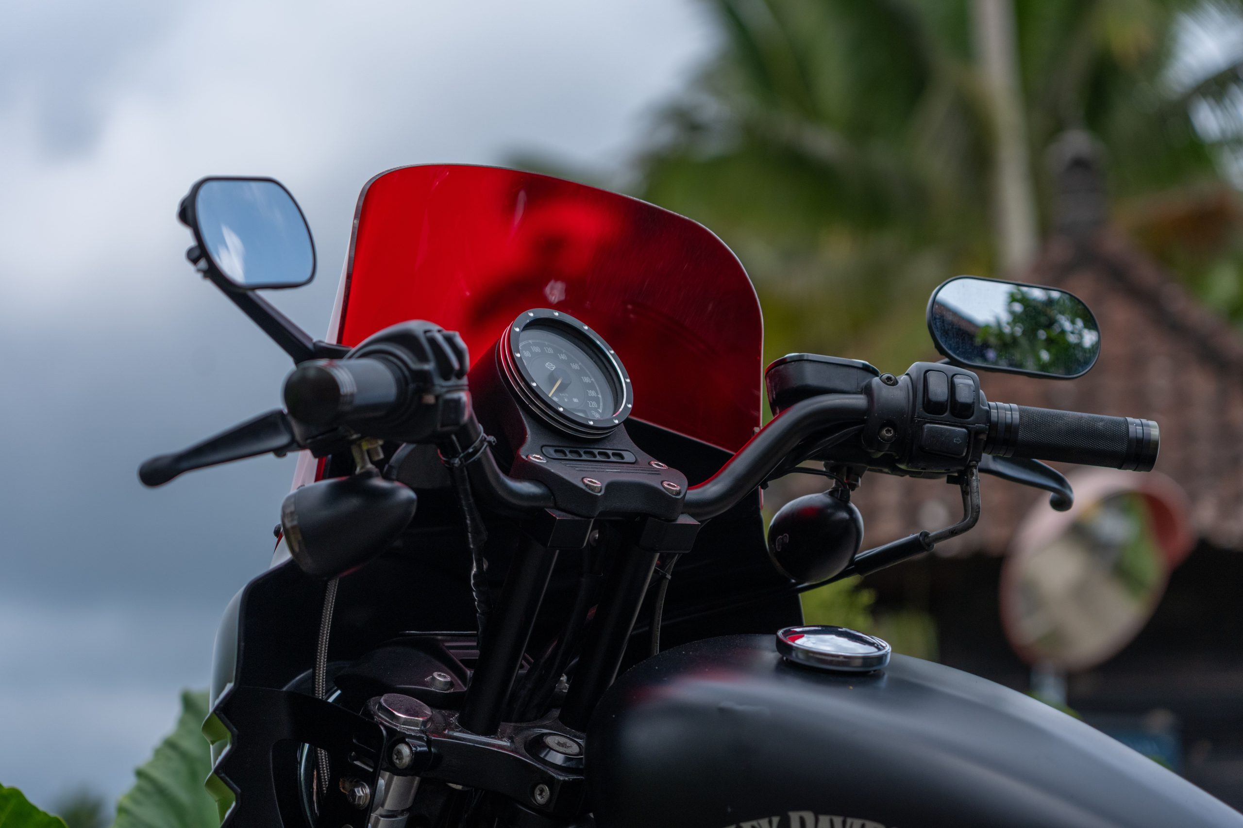 Close-up of motorcycle handlebars and a red-tinted windshield outdoors
