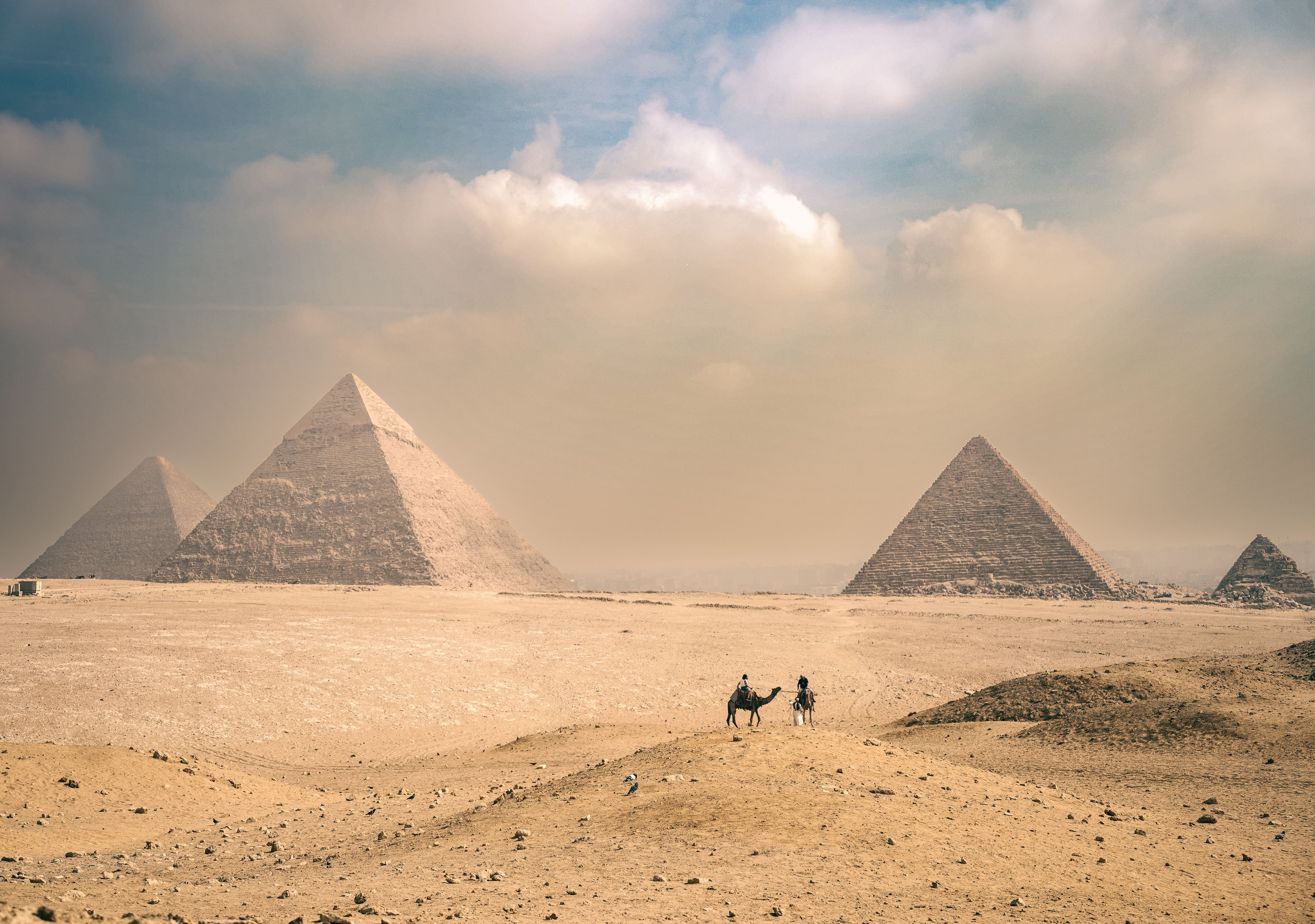 The Great Pyramids of Giza under a sunny sky with travelers on camels in the Egyptian desert