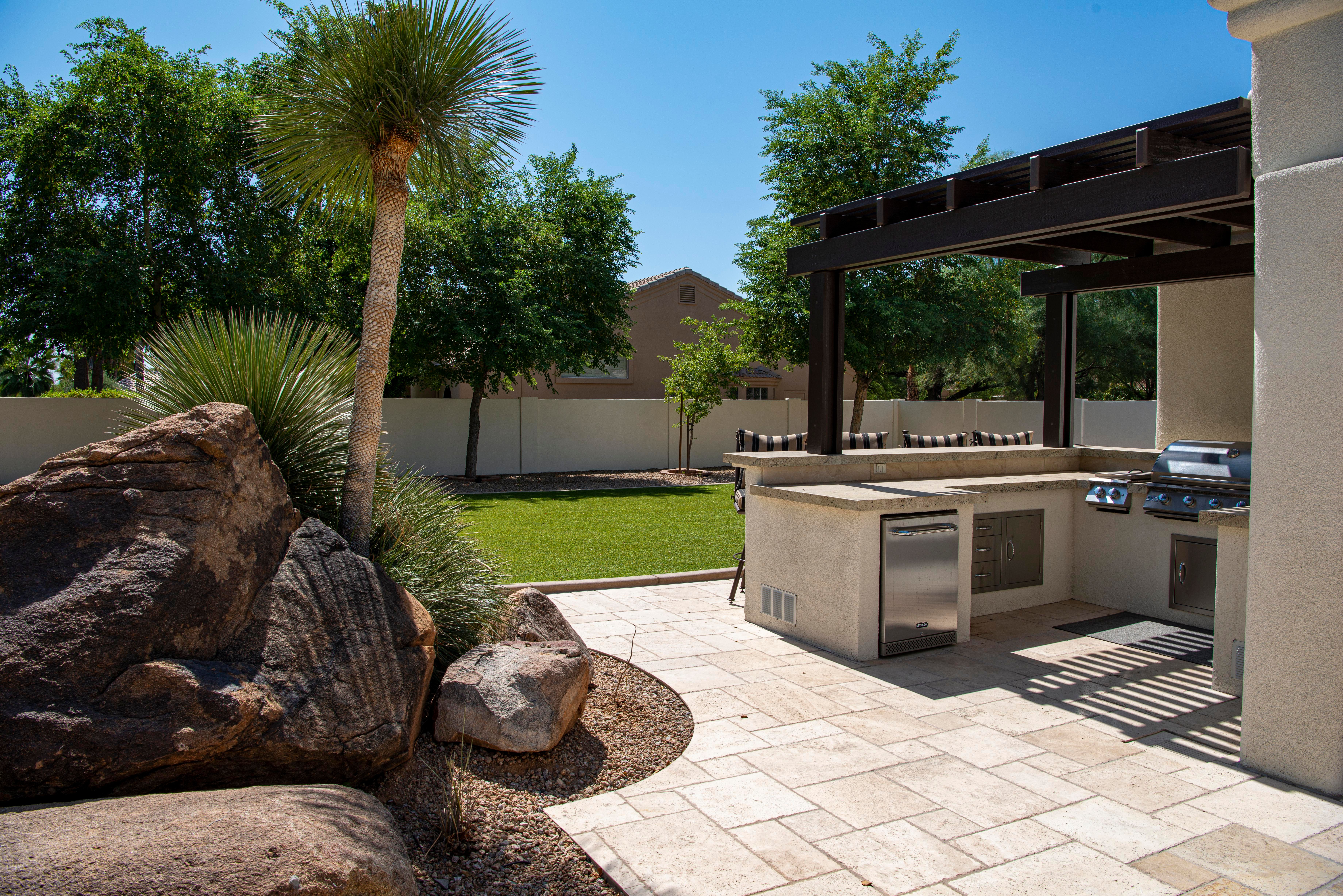 Stylish outdoor kitchen on a sunny patio surrounded by lush landscaping