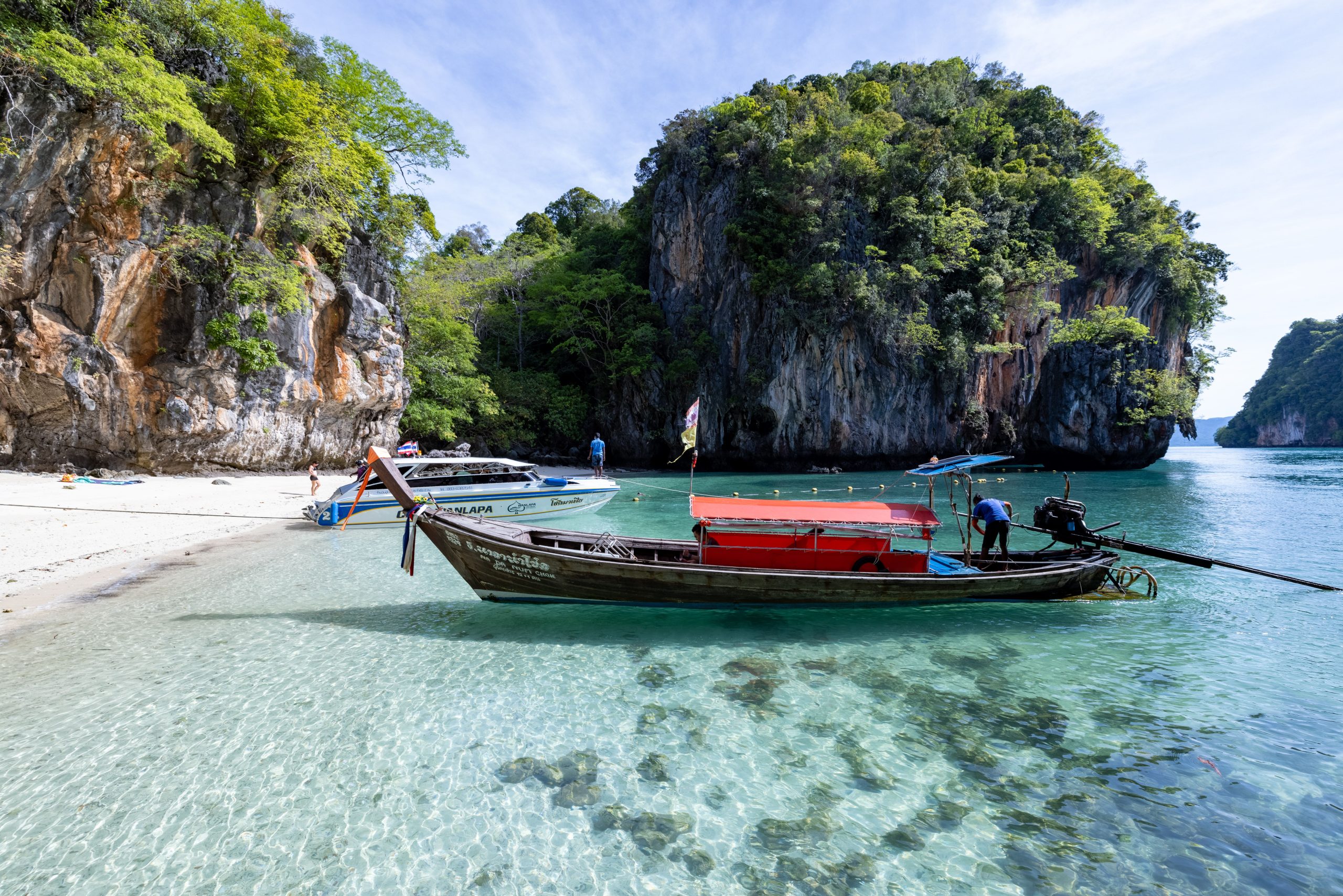Traditional Thai longtail boat on a turquoise beach with limestone cliffs in Krabi, Thailand, a sunny winter escape outside Europe